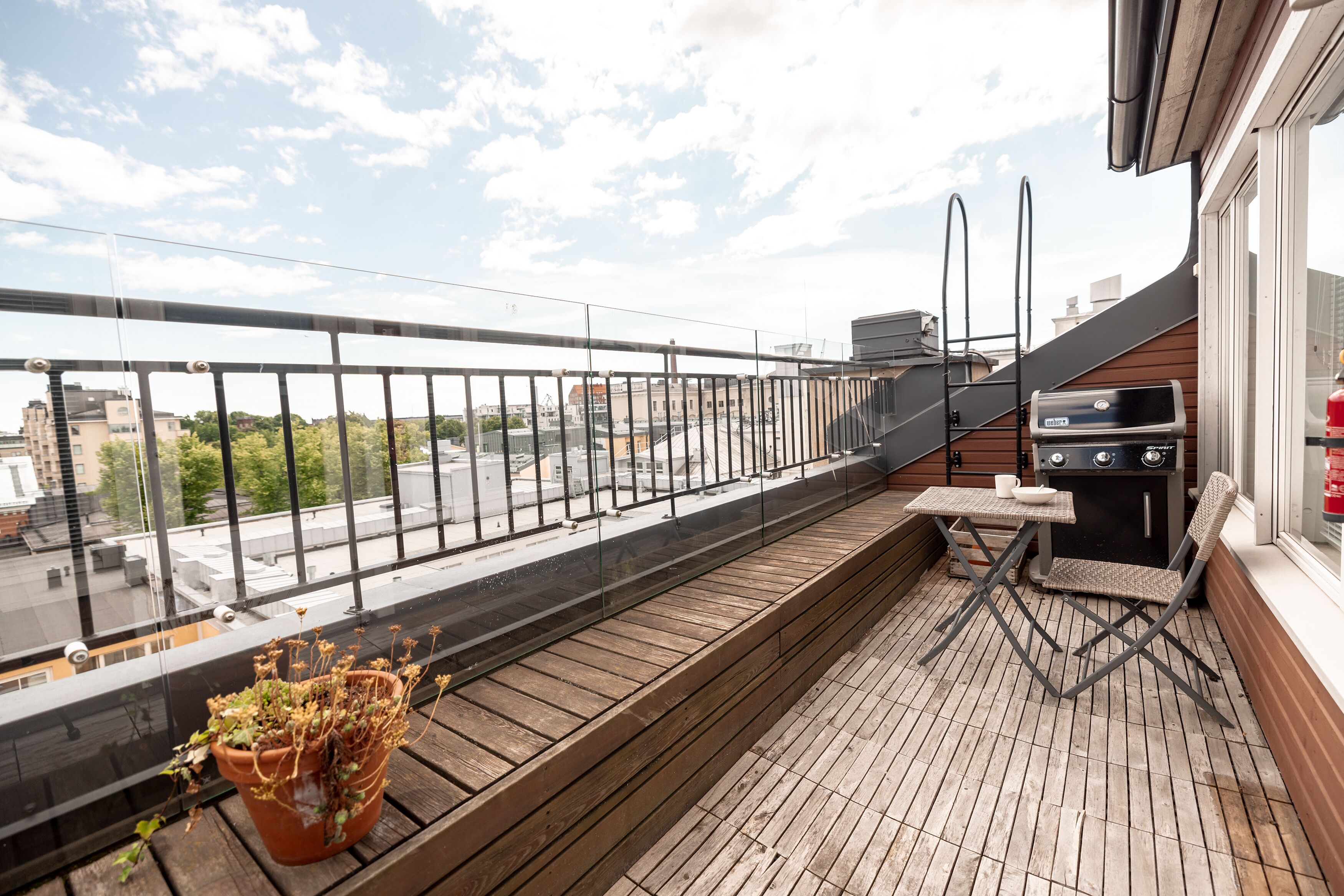 Un balcon doté d’un plancher en bois, d’une plante en pot, d’un barbecue et offrant une vue sur le paysage urbain.