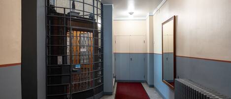 A hallway with a red carpet, a metal cage structure, and a radiator.