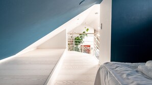 A bedroom with a sloped ceiling, a bed, and a view of a balcony with plants. - 2ndhomes 2BR Penthouse w Terrace&Sauna (Helsinki)