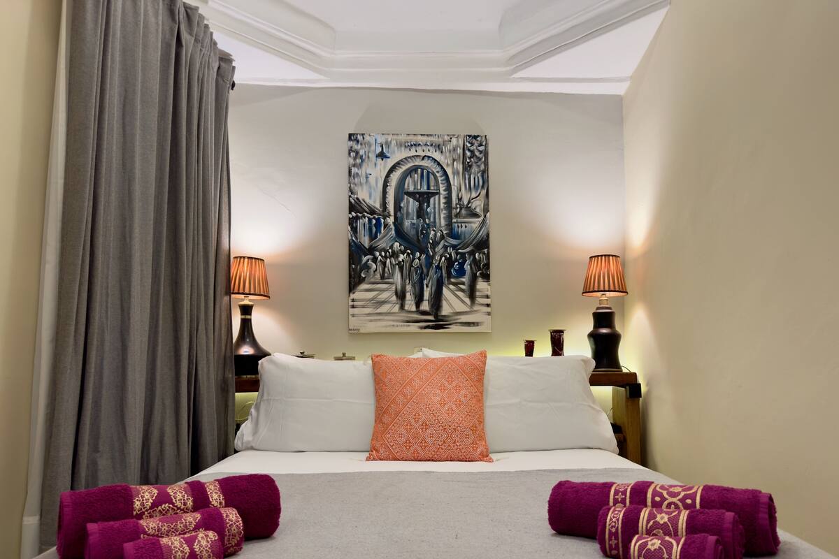 A hotel room with a bed, two lamps, a painting on the wall, and a curtain.