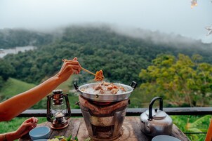 A person cooking outdoors with a portable stove, surrounded by a scenic view of a forested area.