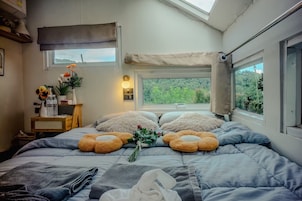 A bedroom with a bed, pillows, a bedside table with a lamp, a window with a view, and a skylight.