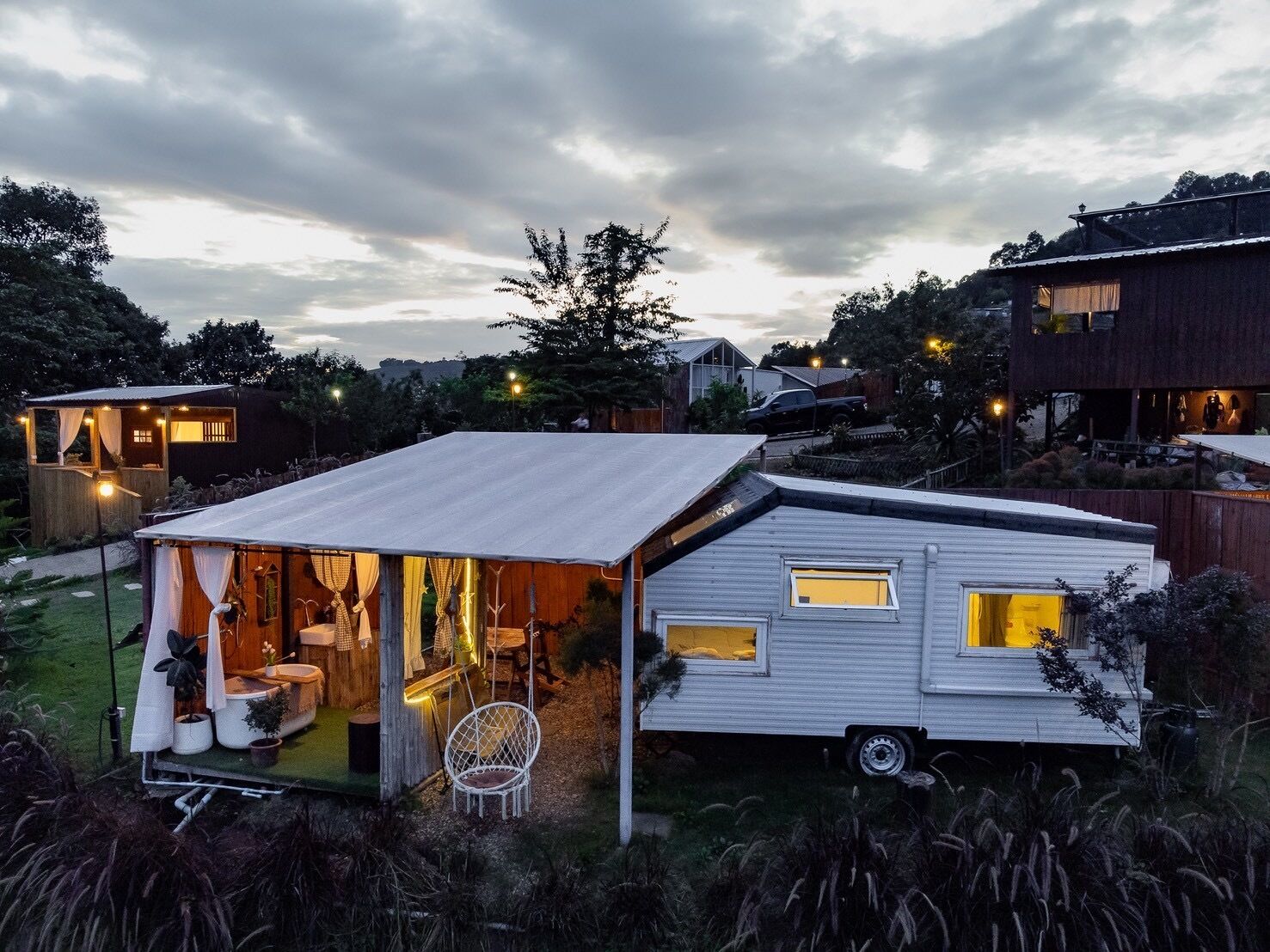 A modern mobile home with a covered porch, a small attached structure, and a garden area.