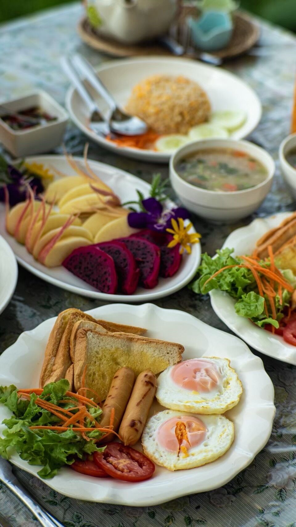 A table with various dishes including a plate with eggs, a bowl of soup, and a plate with sliced vegetables and meat.