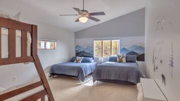 A bedroom with two beds, a ceiling fan, a window with a view of trees, and a wall with a mountain landscape mural.