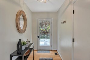 A hallway with a wooden-framed mirror, a console table with a vase and a sculpture, a door with a glass panel, and a small rug on the floor. - Spacious, private, four-season mountainside home close to Wintergreen and hiking (Roseland)