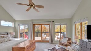 Une chambre à coucher comprenant un lit, une commode en bois, un tapis en peau de vache, un téléviseur et un balcon avec vue sur les arbres.