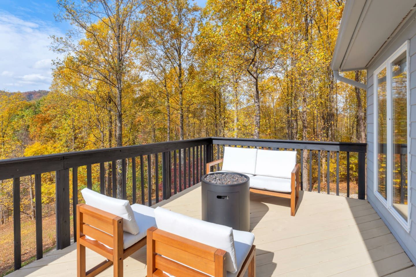 A deck with a sofa and chairs, a fire pit, and a view of autumn trees.