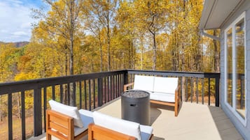 A deck with a sofa and chairs, a fire pit, and a view of autumn trees.