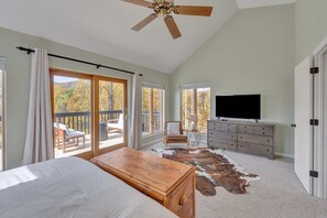 Relax in this serene bedroom with a large bed, ceiling fan, and flat-screen TV, offering a view of the surrounding landscape from the balcony.