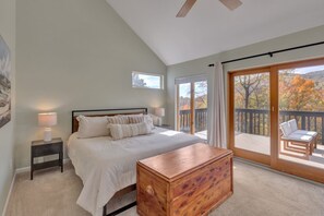 A bedroom with a bed, bedside tables, a wooden chest, a balcony with a chair, and a view of autumn trees. - Spacious, private, four-season mountainside home close to Wintergreen and hiking (Roseland)