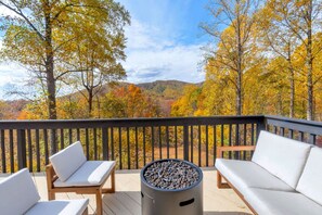 A deck with outdoor seating and a fire pit, overlooking a forested area with autumn foliage. - Spacious, private, four-season mountainside home close to Wintergreen and hiking (Roseland)