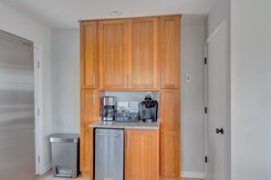 A compact kitchen with wooden cabinets, a stainless steel dishwasher, and a coffee maker.