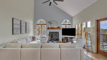 A spacious living room with a large sectional sofa, a fireplace, a flat-screen TV, and a ceiling fan.