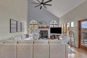 A spacious living room with a large sectional sofa, a fireplace, a flat-screen TV, and a ceiling fan. - Spacious, private, four-season mountainside home close to Wintergreen and hiking (Roseland)
