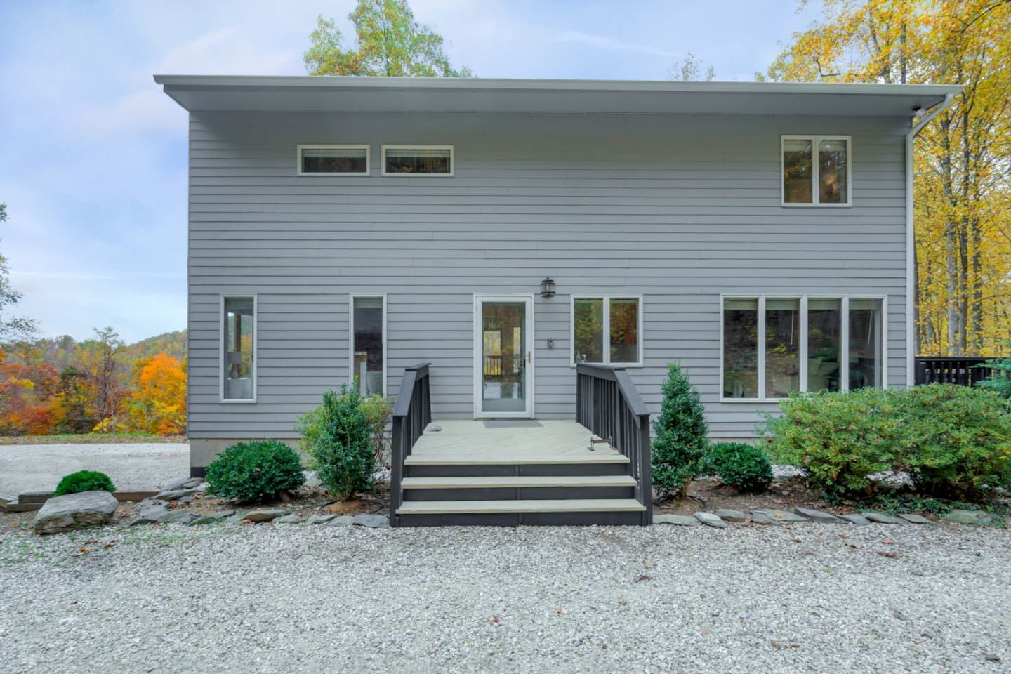 A two-story house with a front porch, a small front yard, and a gravel driveway.