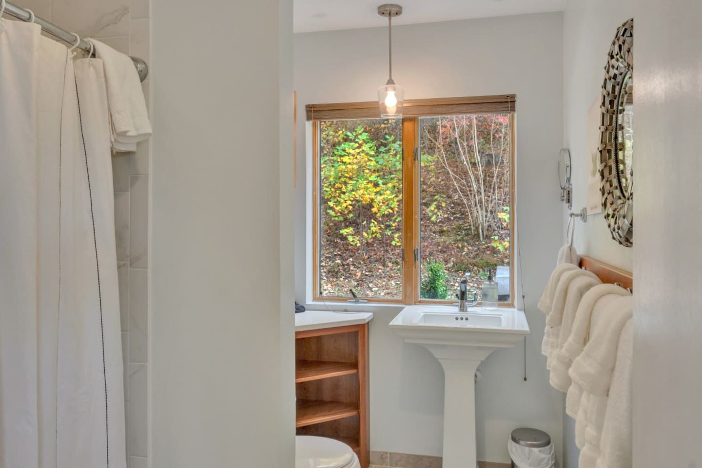 A bathroom with a shower curtain, a sink, a window with a view of trees, and a towel rack.