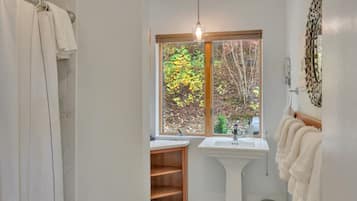 A bathroom with a shower curtain, a sink, a window with a view of trees, and a towel rack.
