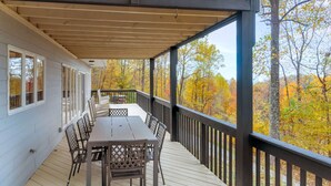 Une terrasse couverte, dotée d’une table et de chaises, qui offre une vue sur une forêt aux couleurs automnales.
