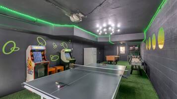 Ein Raum mit Tischtennisplatte, zwei Spielautomaten und einem Kicker.