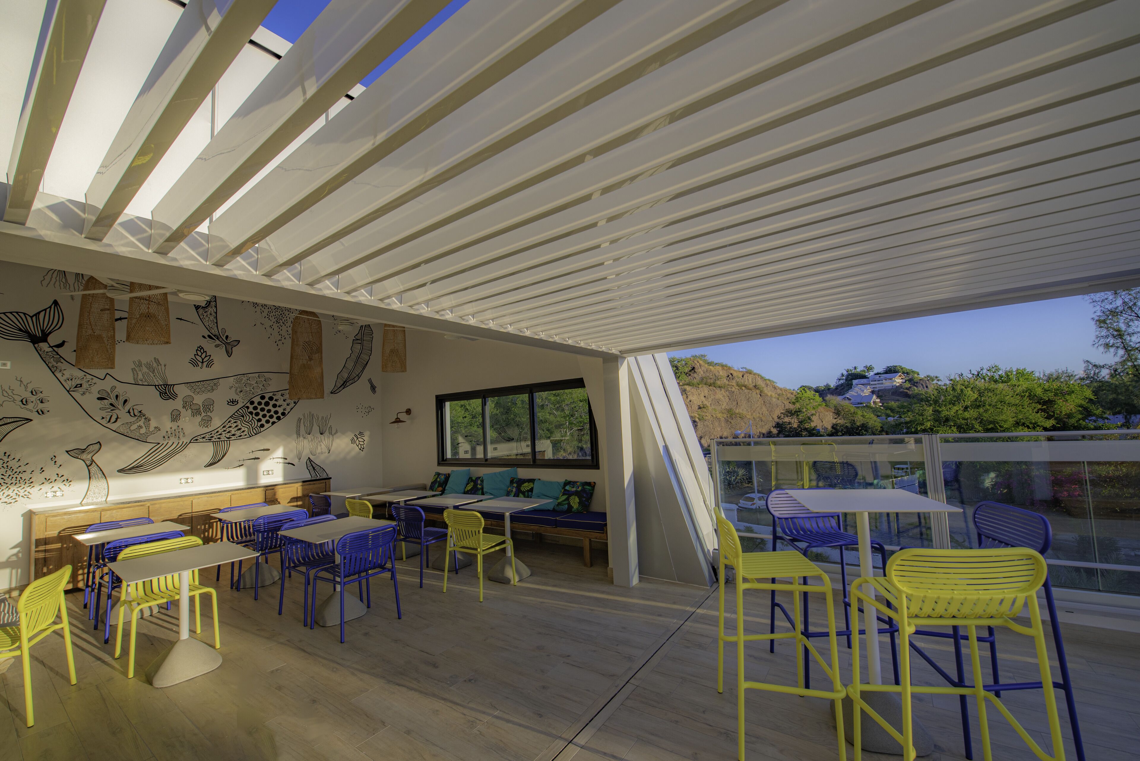 A modern dining area with a high ceiling, a mural, and a view of the outdoors.