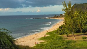 A beach with people relaxing, a lighthouse in the distance, and lush greenery. - Boutik Hotel 2A (Saint-Paul)