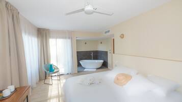 Une chambre d’hôtel avec un grand lit, un ventilateur de plafond, une salle de bain avec baignoire et un fauteuil.
