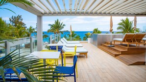 A covered outdoor area with lounge chairs, a table, and a view of the ocean. - Boutik Hotel 2A (Saint-Paul)