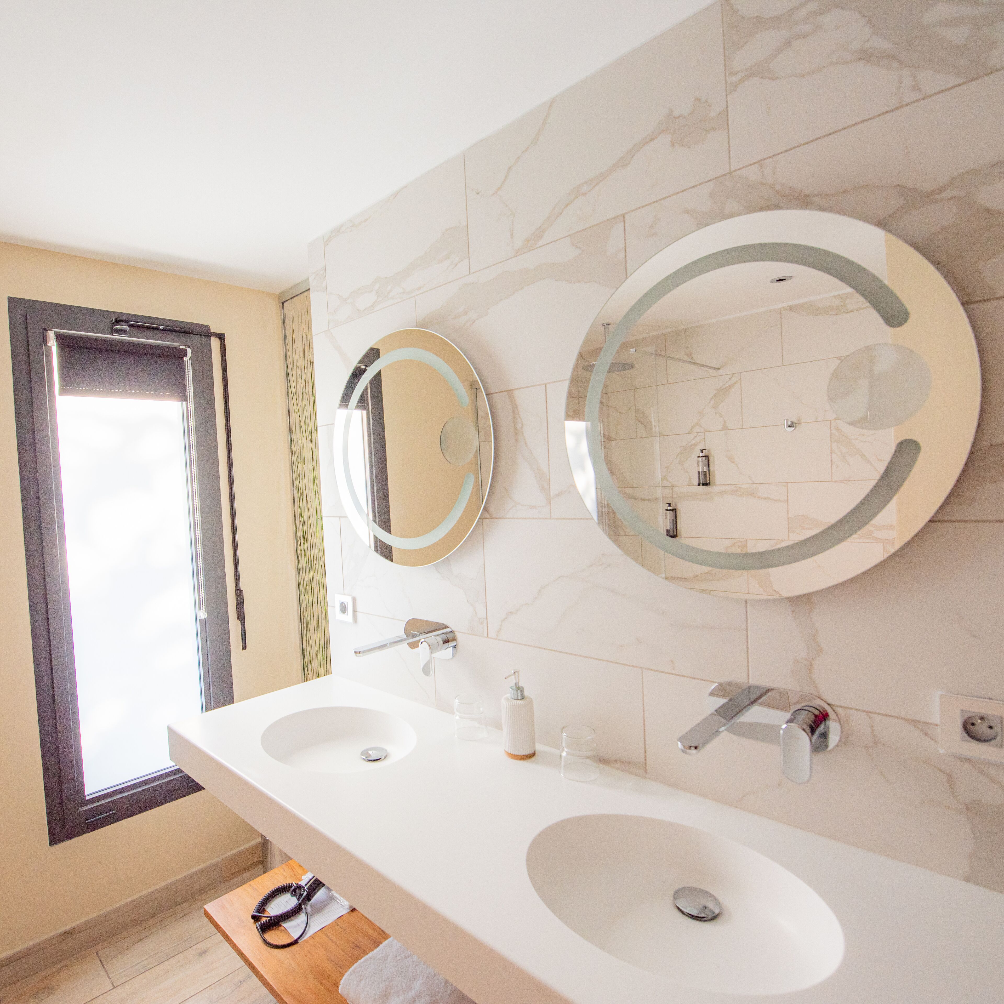 Une salle de bain avec deux lavabos, un grand miroir et une fenêtre.