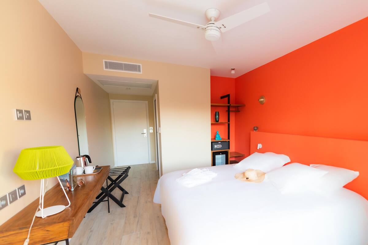 A hotel room with a bed, a desk, a bright lamp, a ceiling fan, and a red accent wall.