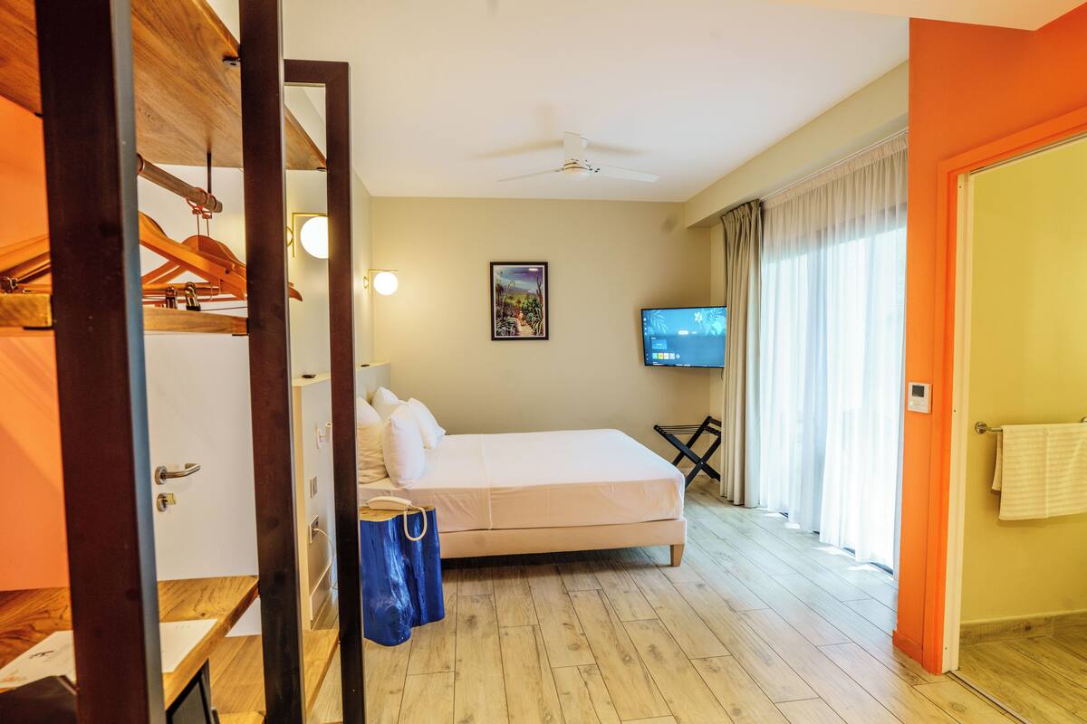 A hotel room with a bed, a television, a ceiling fan, and a window with curtains.