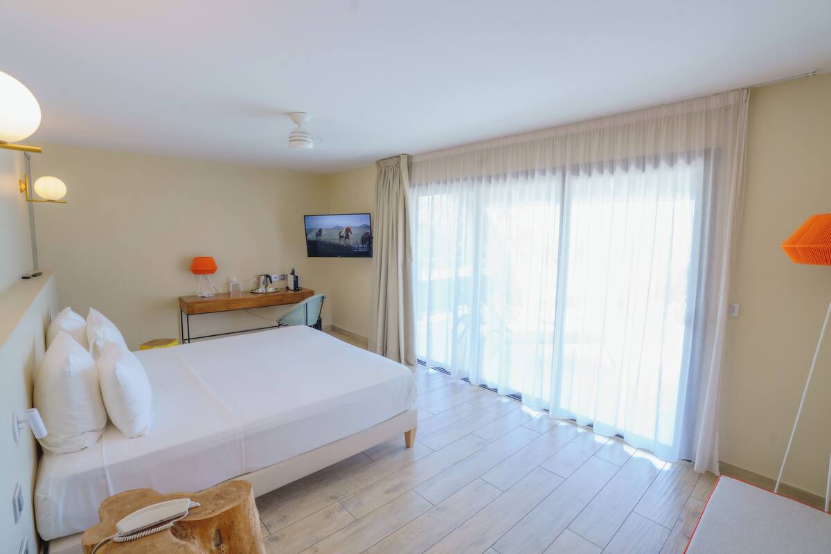 A hotel room with a large bed, a television on the wall, a desk with a chair, and a window with curtains.