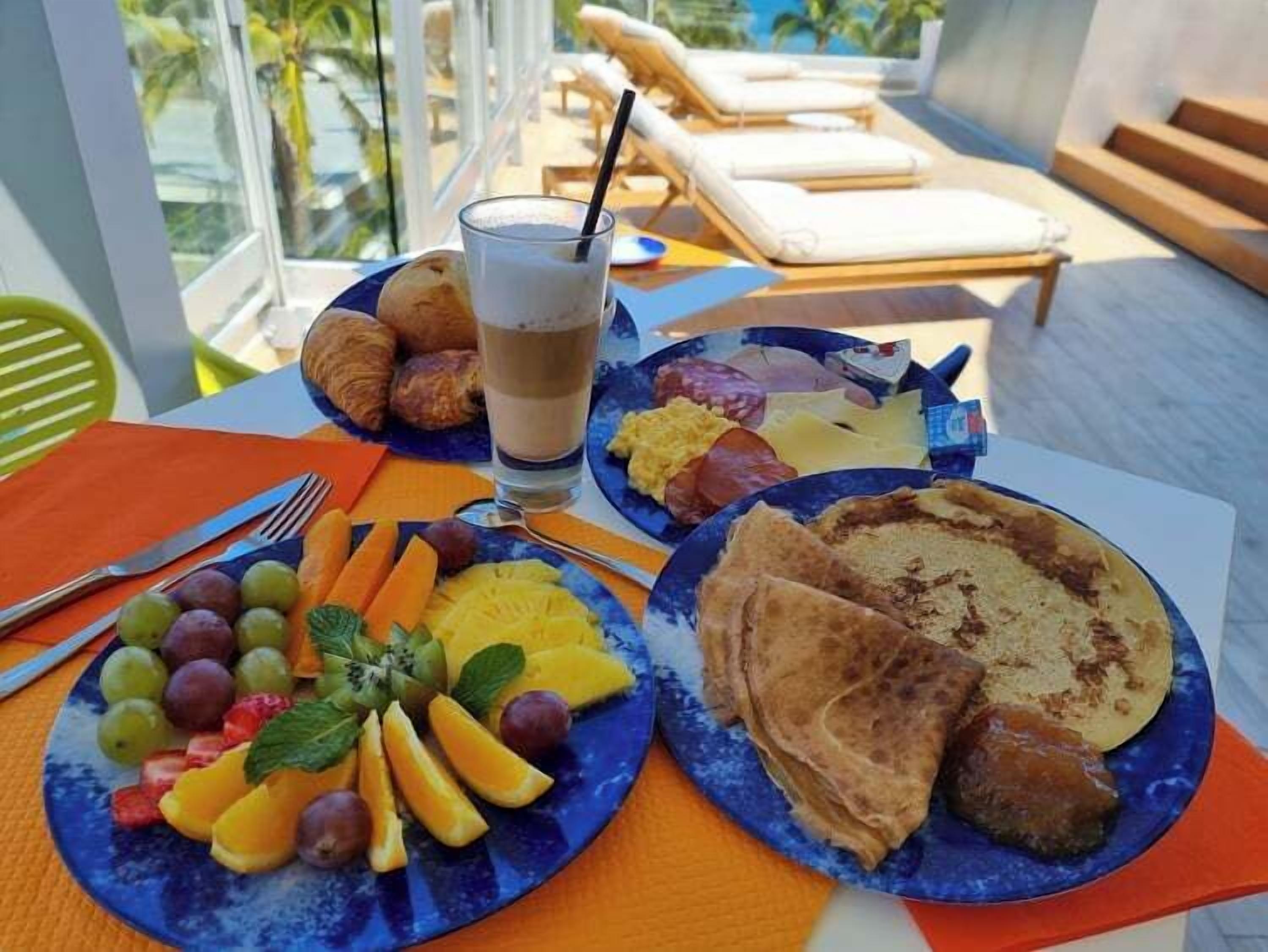 A breakfast setting with plates of fruit, toast, and croissants on a table with a view of a pool and lounge chairs.