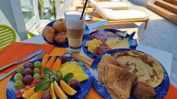 A breakfast setting with plates of fruit, toast, and croissants on a table with a view of a pool and lounge chairs.