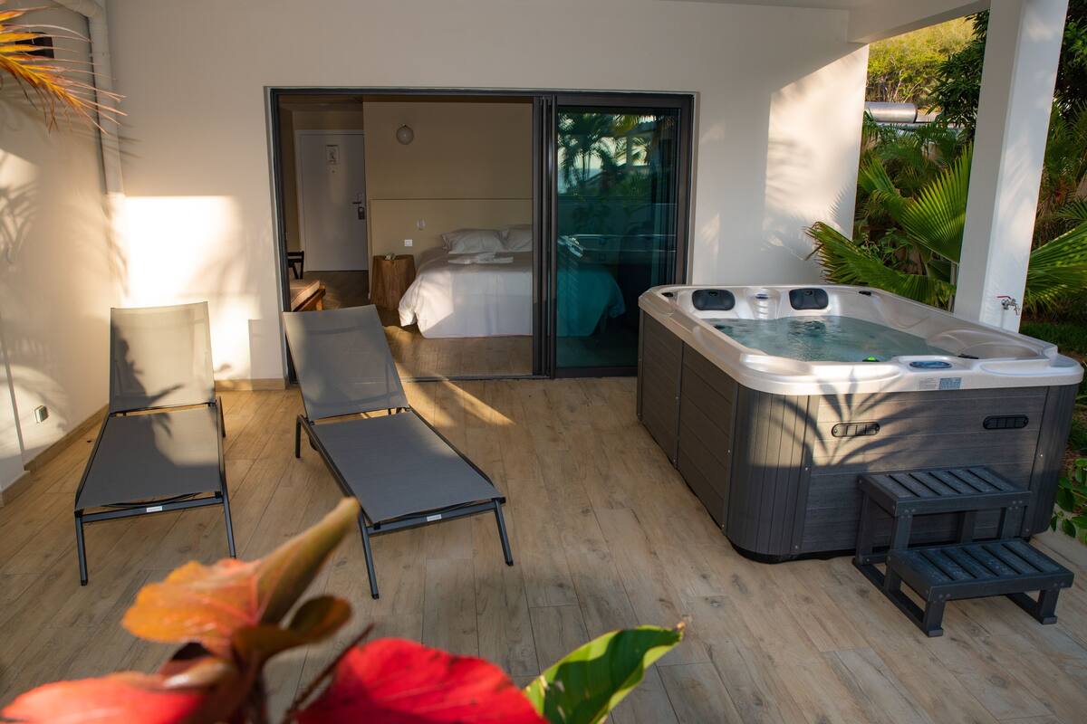 A modern outdoor lounge area with a hot tub, two lounge chairs, and a sliding glass door leading to a bedroom.