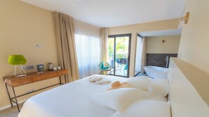 A hotel room with a large bed, a desk with a lamp, a bathroom with a bathtub, and a view of the outdoors. - Boutik Hotel 2A (Saint-Paul)
