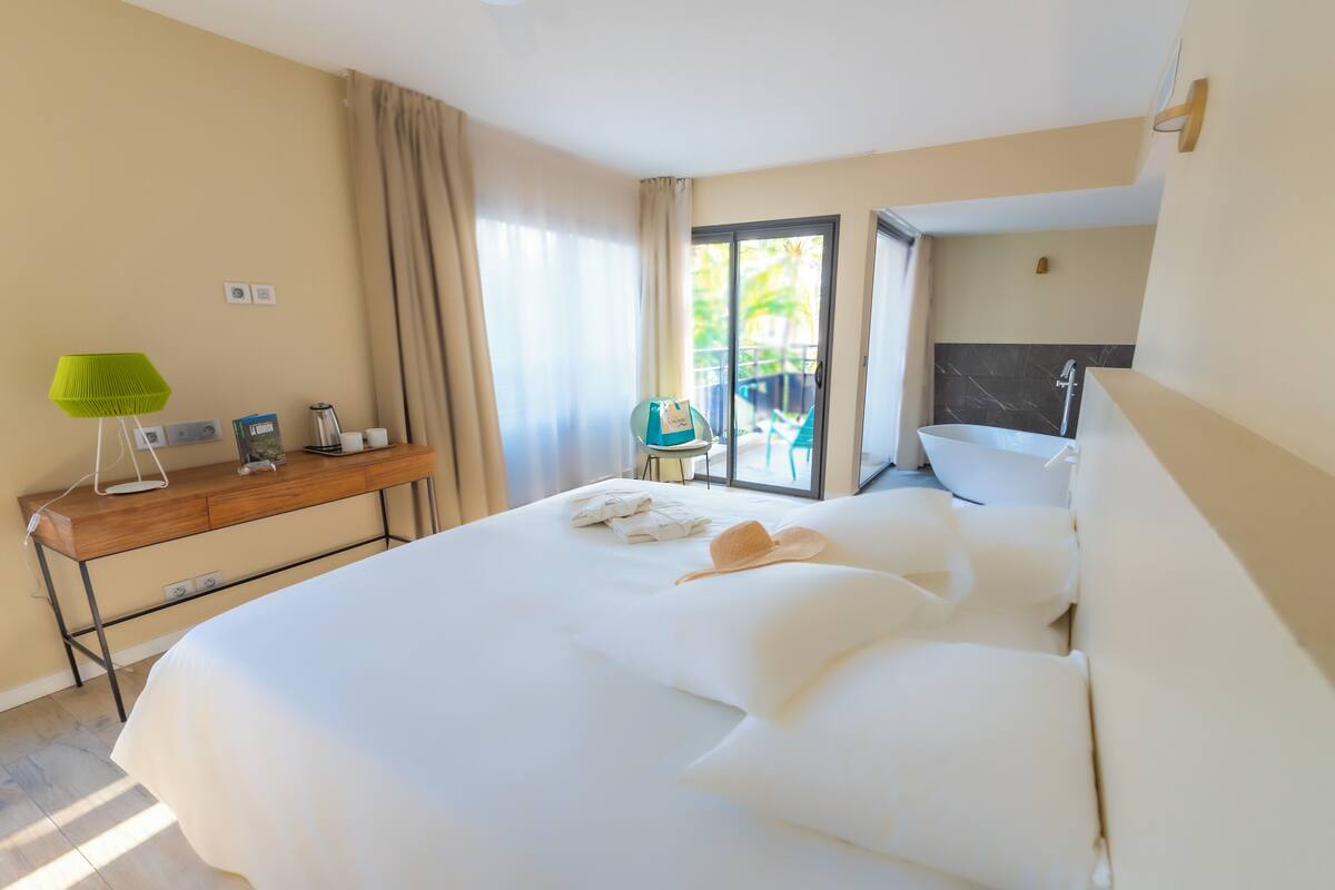 A hotel room with a large bed, a desk with a lamp, a bathroom with a bathtub, and a view of the outdoors.