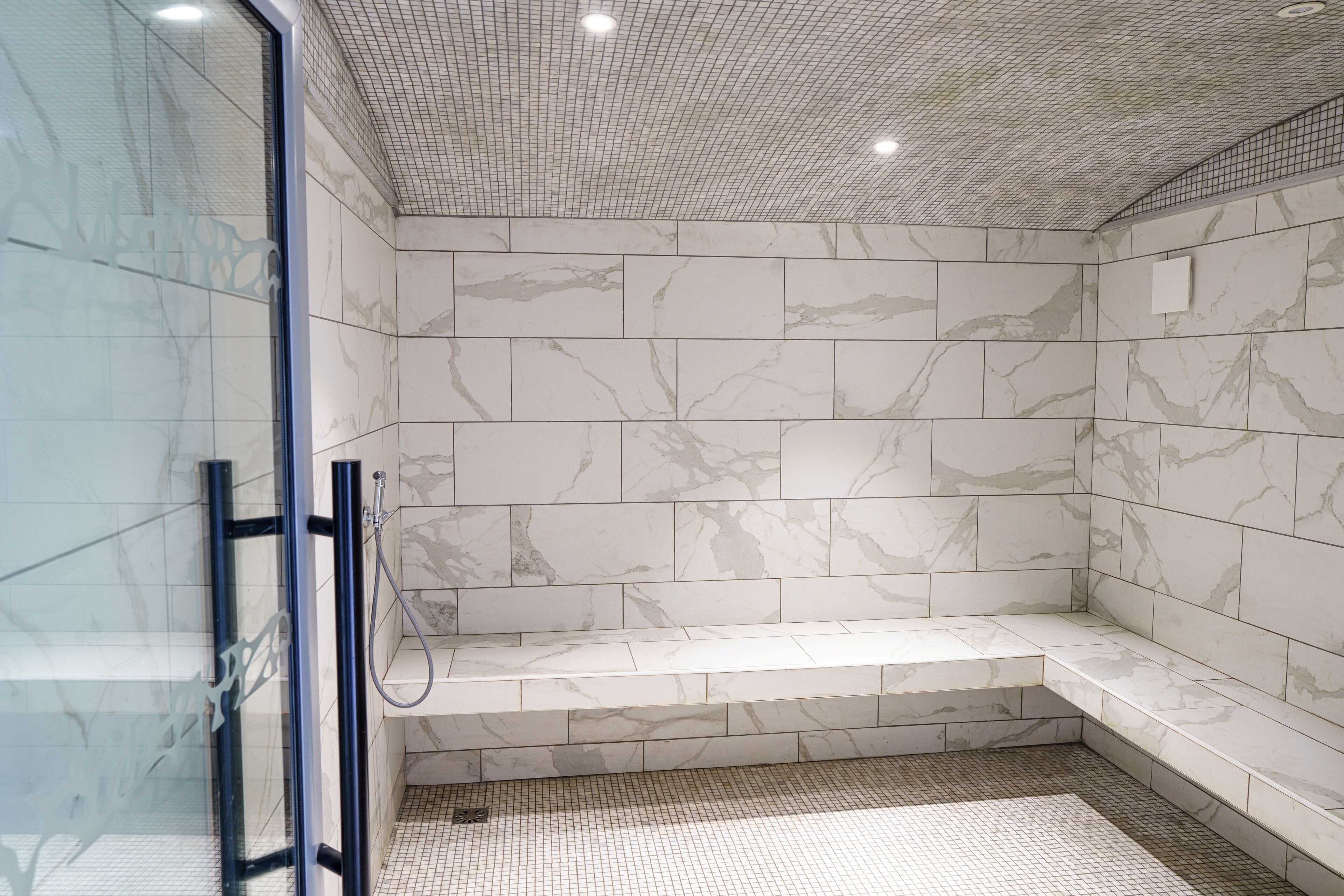 A modern shower area with a glass door, marble tiles, and a bench.