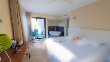 Una habitación de hotel con una cama, un escritorio con lámpara, una silla, un baño con bañera y un ventilador de techo.
