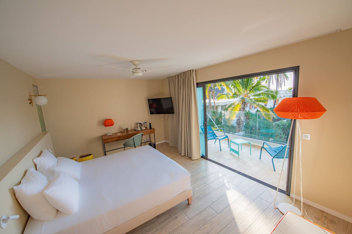 A hotel room with a bed, a desk, a TV, and a balcony with chairs and a table.