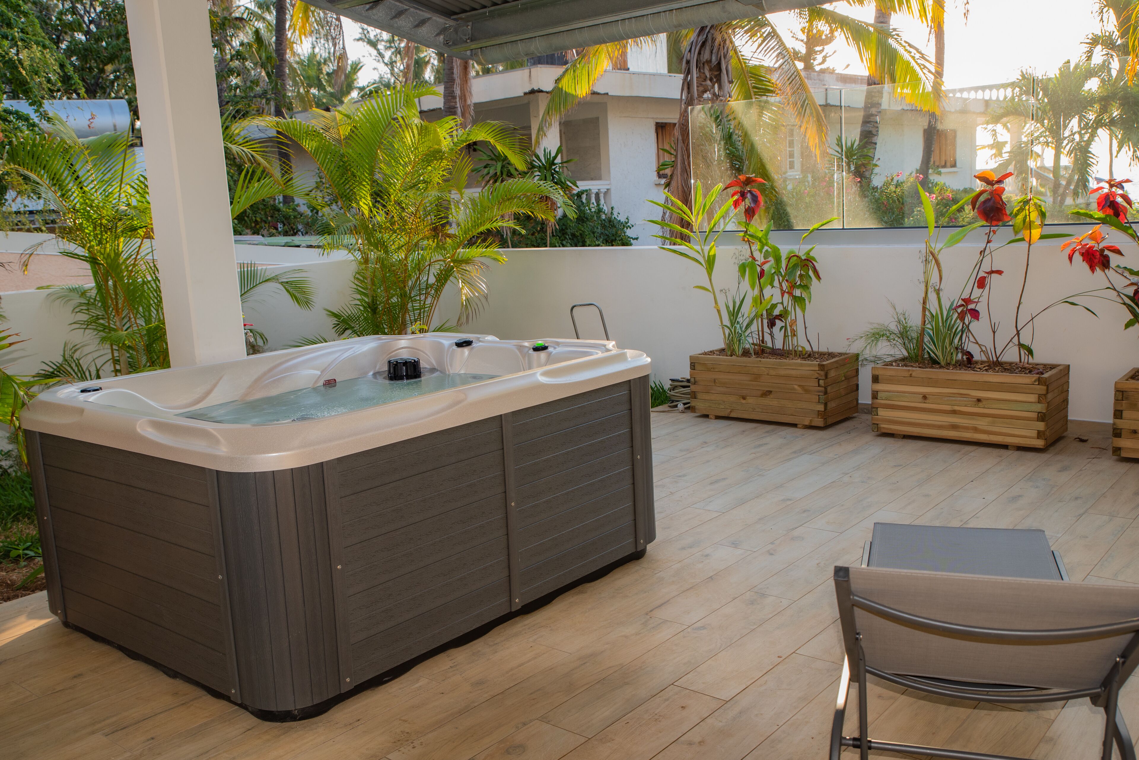 Un jacuzzi en un patio exterior con suelo de madera, rodeado de plantas en macetas y vista a un edificio residencial.