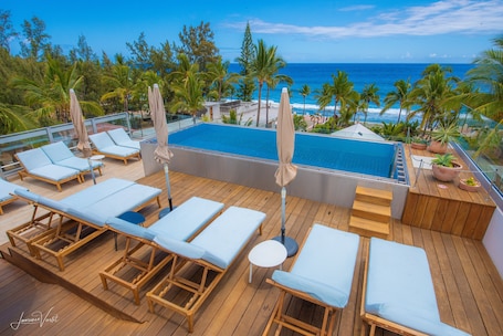 A rooftop pool area with lounge chairs and umbrellas, overlooking a beach and ocean.