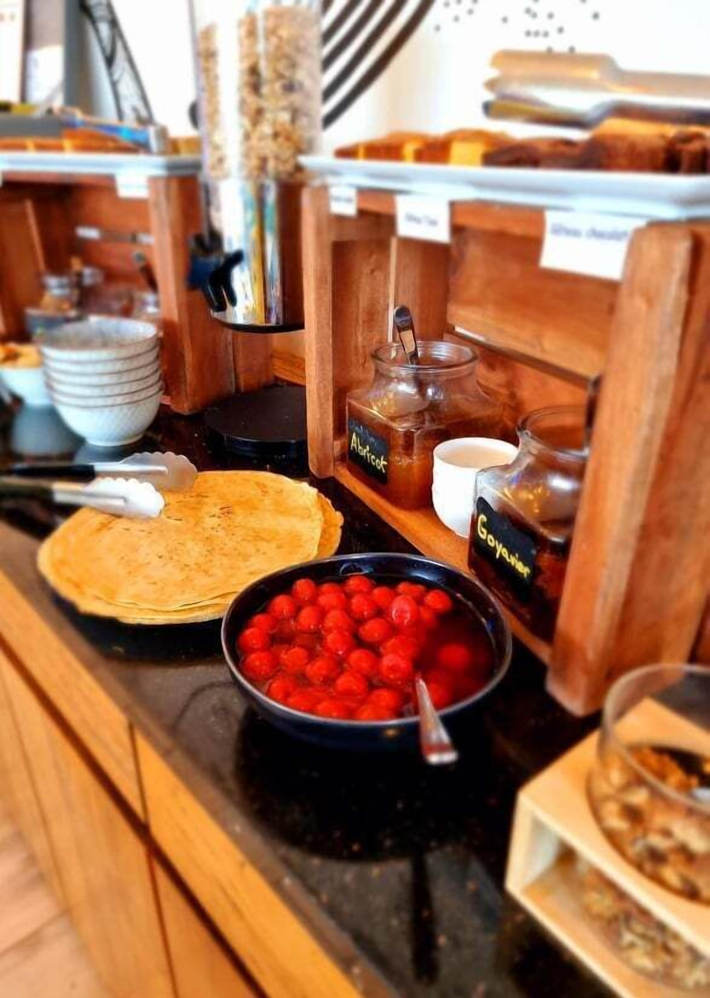 A breakfast buffet with various food items including pancakes, a bowl of berries, and a jar of jam.