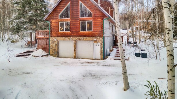 A wooden cabin with a stone foundation, a garage, and a small deck.