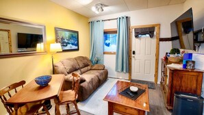 A compact living space with a sofa, a dining table with chairs, a small kitchen area, and a door leading to another room.