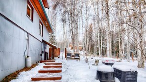 A residential building with a metal exterior, wooden steps leading to a garage, and a snow-covered yard with trees.