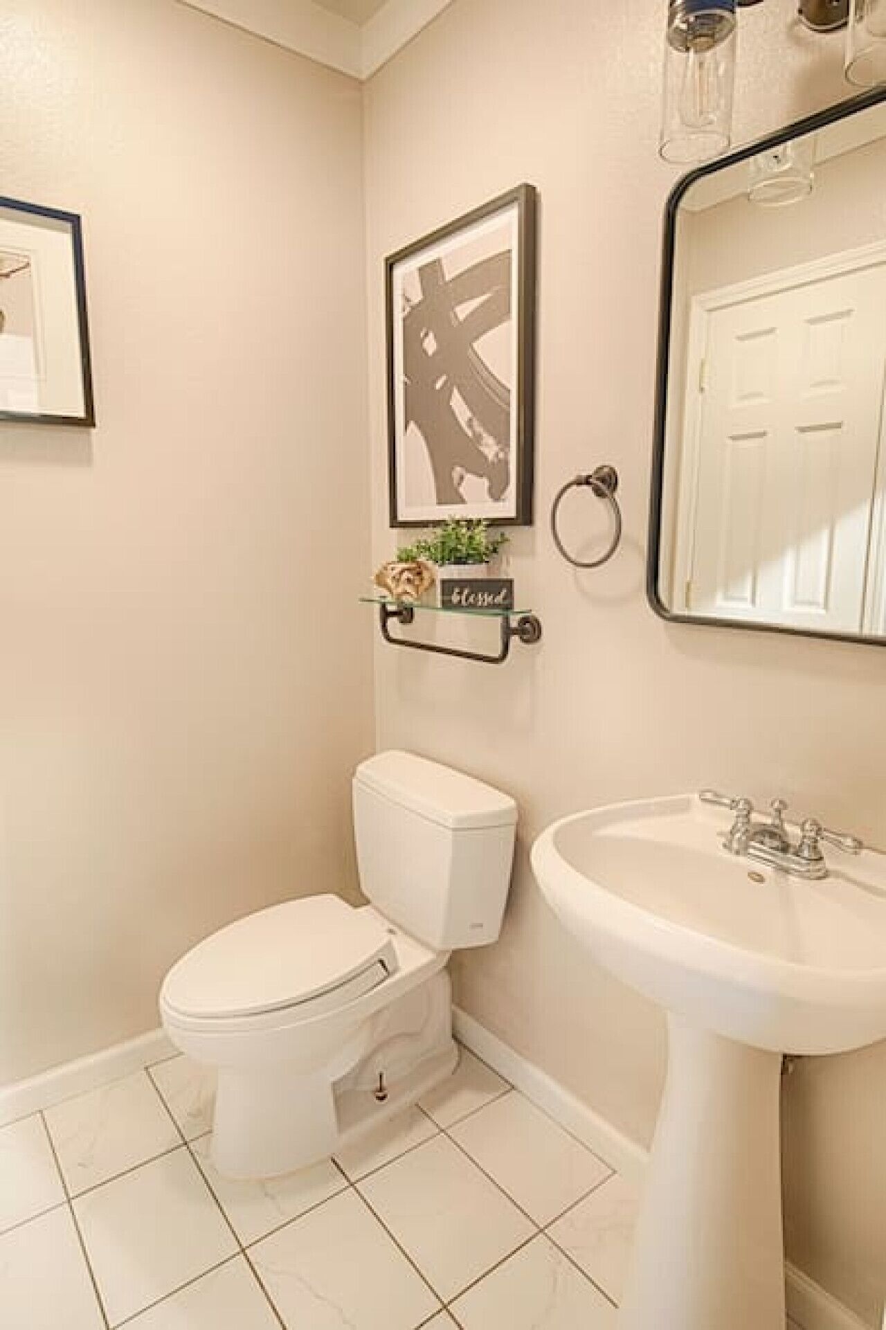 A bathroom with a toilet, sink, and a framed artwork on the wall.