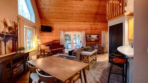 Een gezellig cabin interieur met een houten eettafel, een piano, een bank en een keuken met een stenen aanrecht.