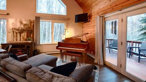 Een gezellige woonkamer met een vleugelpiano, een groot raam met uitzicht op een besneeuwde bossen en een comfortabele zithoek.