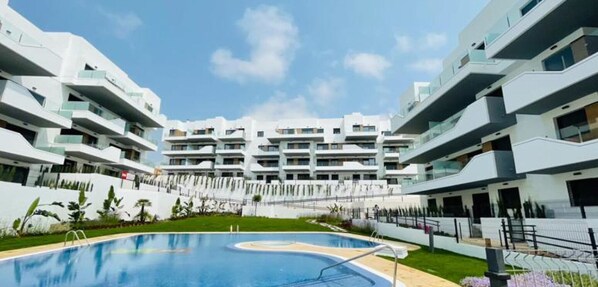 A modern hotel with a central swimming pool, multiple balconies, and a clear sky.